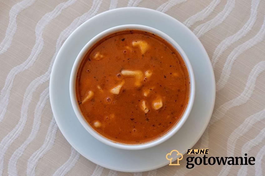 Zupa pomidorowa z lanymi kluskami podana w białej miseczce.