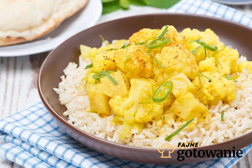 Curry z kalafiorem podane z dodatkiem ryżu w brązowej miseczce.